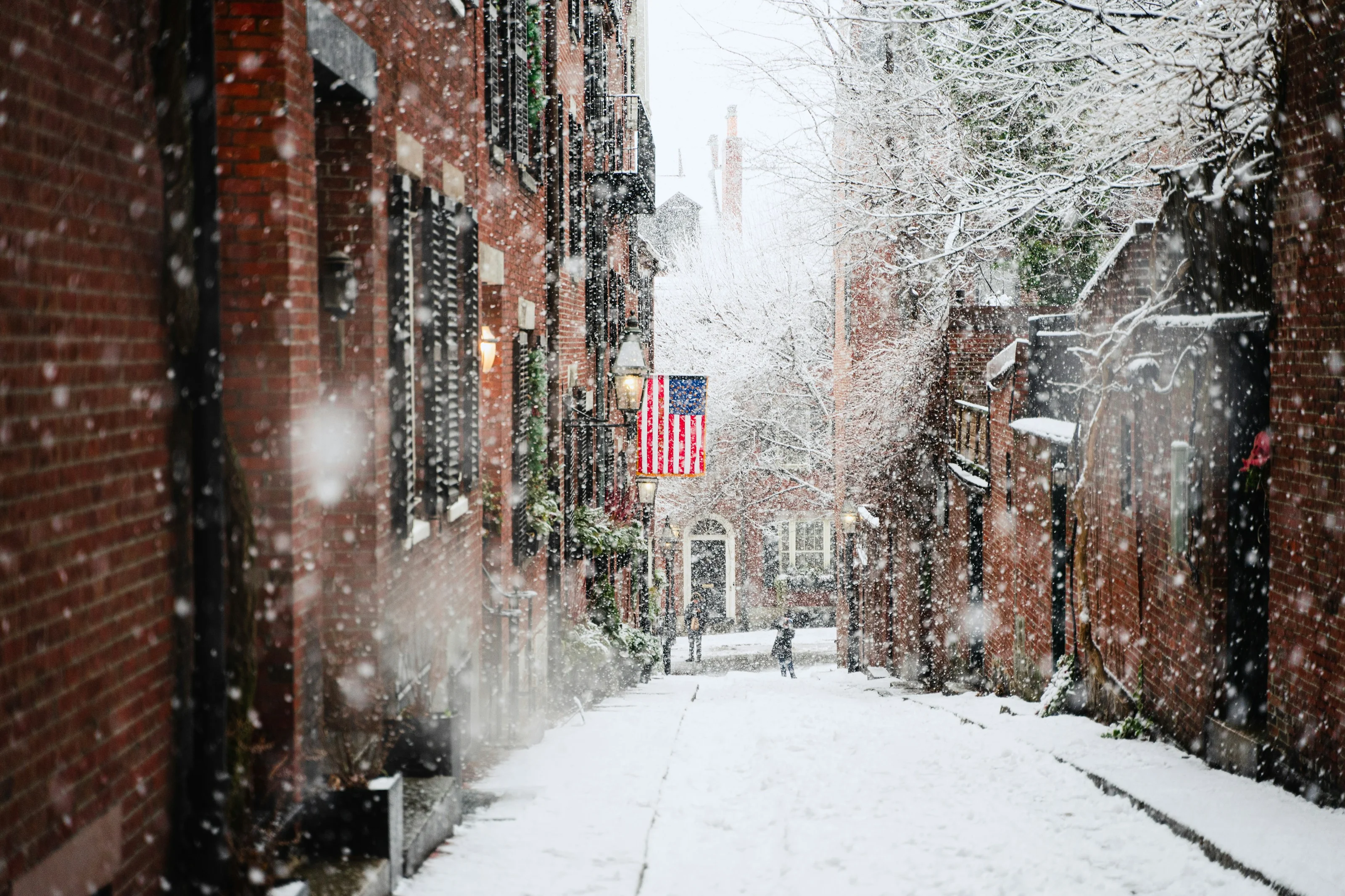 Callejón nevado en Beacon Hill con una bandera de Estados Unidos colgando de una casa de ladrillo